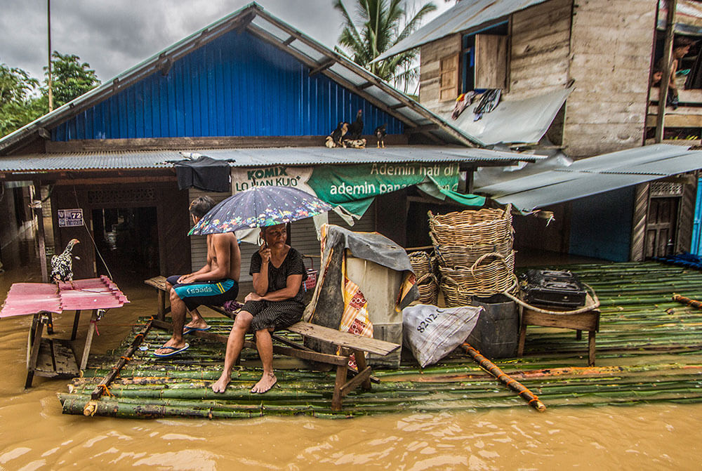 A woman holds an umbrella as she waits with her family to be evacuated by the rescue team on a bamboo raft in front of her flooded house in South Kalimantan, Indonesia.